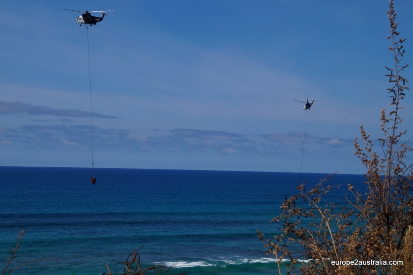 Two helicopters are scooping up ocean water and dumping it on the fire.